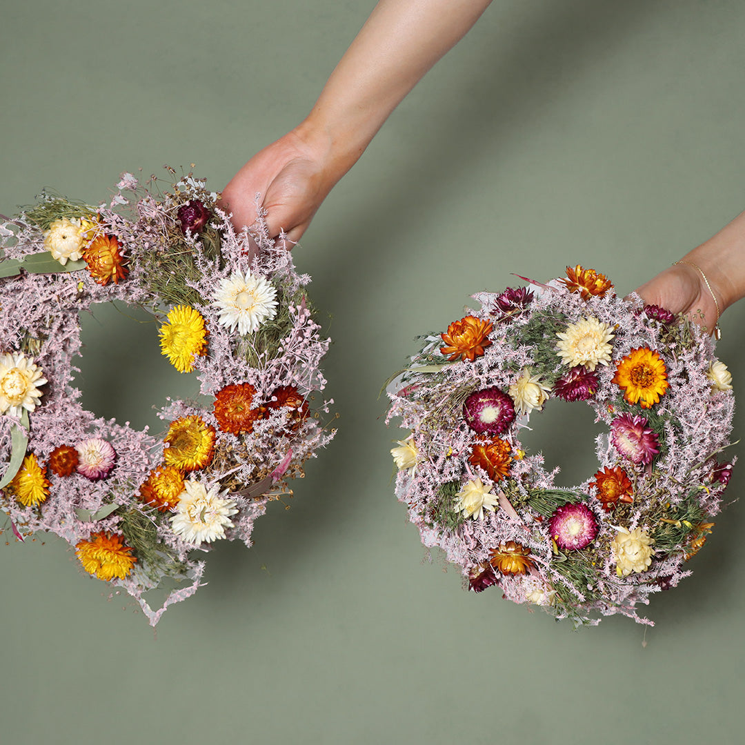 Two hands holding floral wreaths against a green background