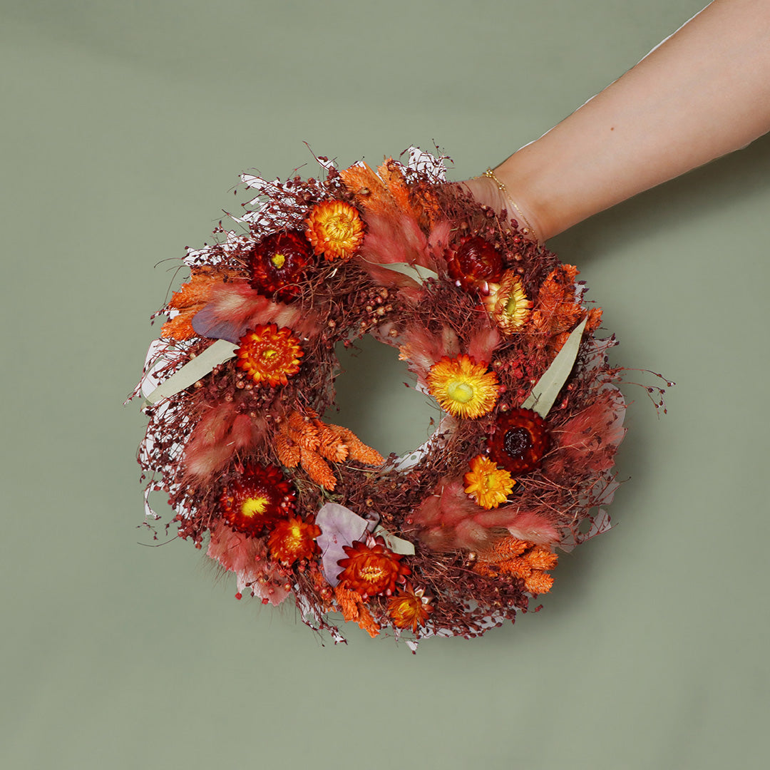 Hand holding a floral wreath with autumn colors against a green background